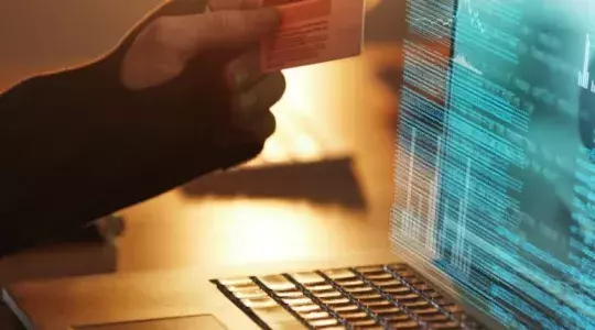 main tenant une carte bleue devant un ordinateur portable piratage